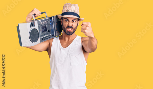 Young hispanic man holding boombox, listening to music annoyed and frustrated shouting with anger, yelling crazy with anger and hand raised
