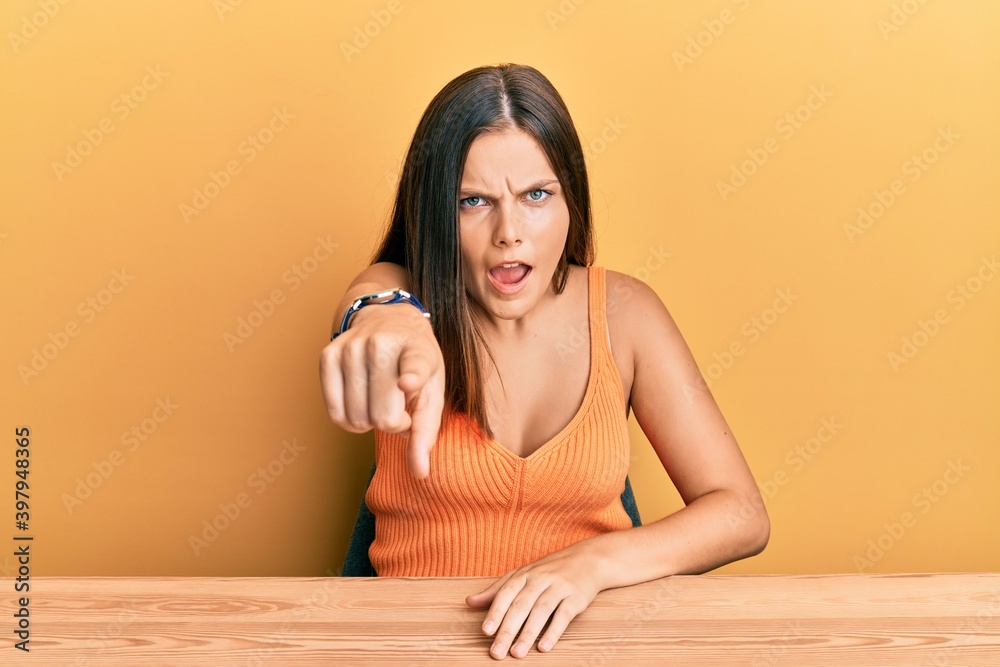 Young caucasian woman wearing casual clothes sitting on the table pointing displeased and frustrated to the camera, angry and furious with you Young caucasian woman wearing casual clothes sitting on the table pointing displeased and frustrated to the camera, angry and furious with you