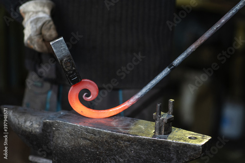  close-up of the hands of a Blacksmith forging a curl from a red-hot flattened blank with a hammer. Handmade in the forge concept photo