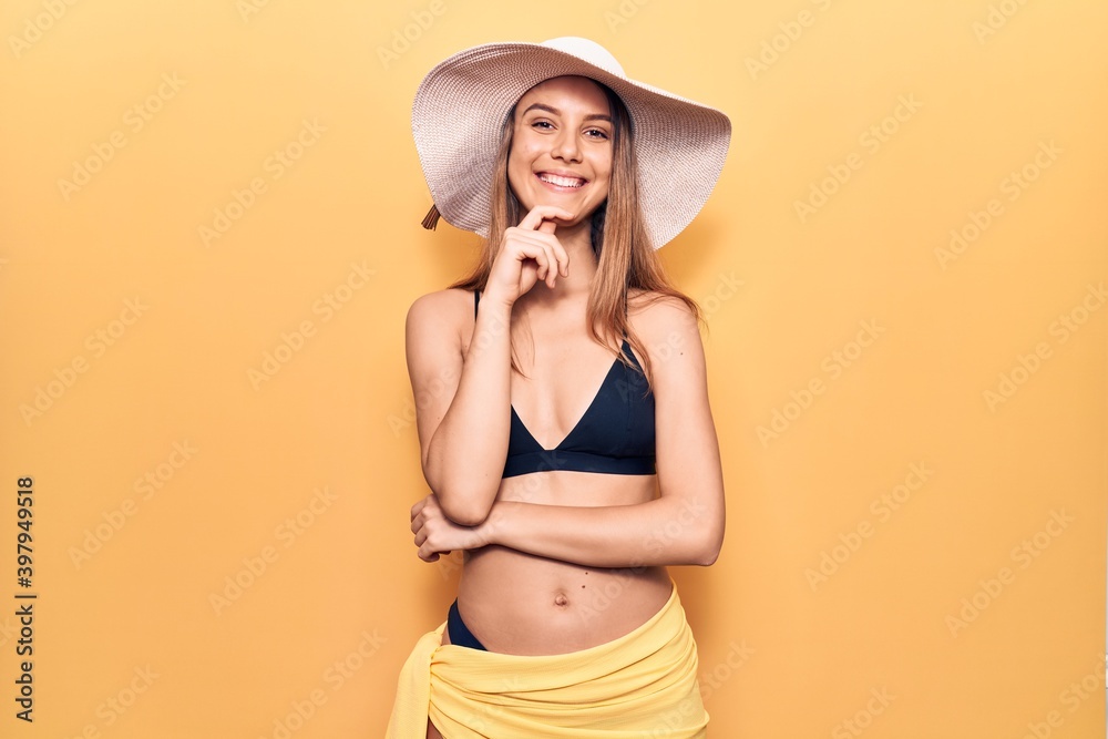 Young beautiful girl wearing bikini and hat smiling looking confident at the camera with crossed arms and hand on chin. thinking positive. Young beautiful girl wearing bikini and hat smiling looking confident at the camera with crossed arms and hand on chin. thinking positive.