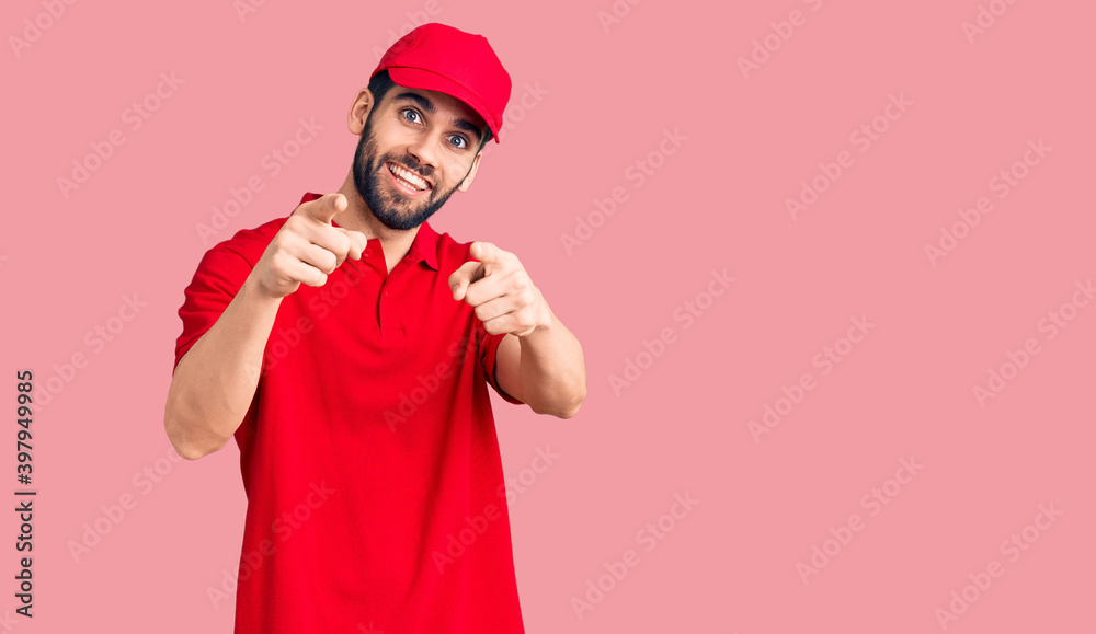 Young handsome man with beard wearing delivery uniform pointing fingers to camera with happy and funny face. good energy and vibes.