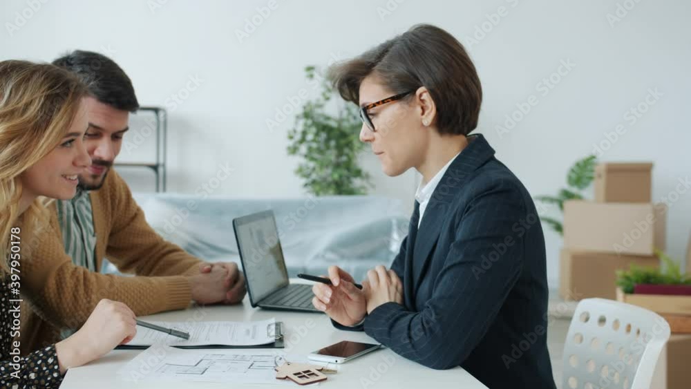 Young family man and woman are discussing sales contract with real estate specialist reading document indoors sitting at table together. People and deals concept. Young family man and woman are discussing sales contract with real estate specialist reading document indoors sitting at table together. People and deals concept.
