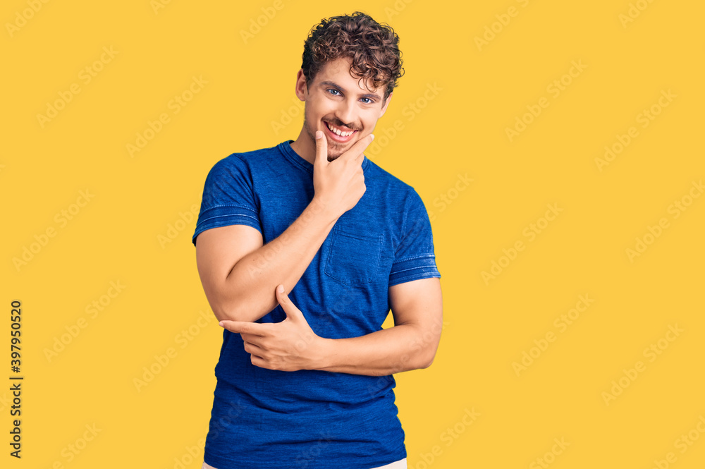 Young handsome man with curly hair wearing casual clothes looking confident at the camera smiling with crossed arms and hand raised on chin. thinking positive. Young handsome man with curly hair wearing casual clothes looking confident at the camera smiling with crossed arms and hand raised on chin. thinking positive.