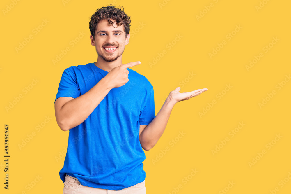 Young handsome man with curly hair wearing casual clothes amazed and smiling to the camera while presenting with hand and pointing with finger. Young handsome man with curly hair wearing casual clothes amazed and smiling to the camera while presenting with hand and pointing with finger.
