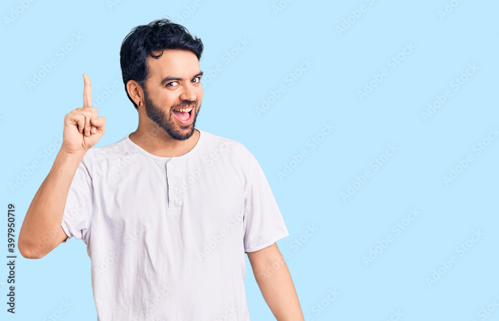 Young hispanic man wearing casual clothes pointing finger up with successful idea. exited and happy. number one. Young hispanic man wearing casual clothes pointing finger up with successful idea. exited and happy. number one.