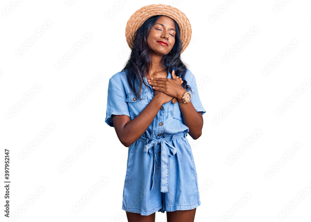 Young indian girl wearing summer hat smiling with hands on chest with closed eyes and grateful gesture on face. health concept. Young indian girl wearing summer hat smiling with hands on chest with closed eyes and grateful gesture on face. health concept.