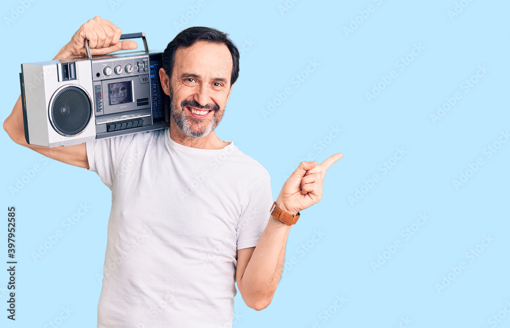 Middle age handsome man listening to music using vintage boombox smiling happy pointing with hand and finger to the side