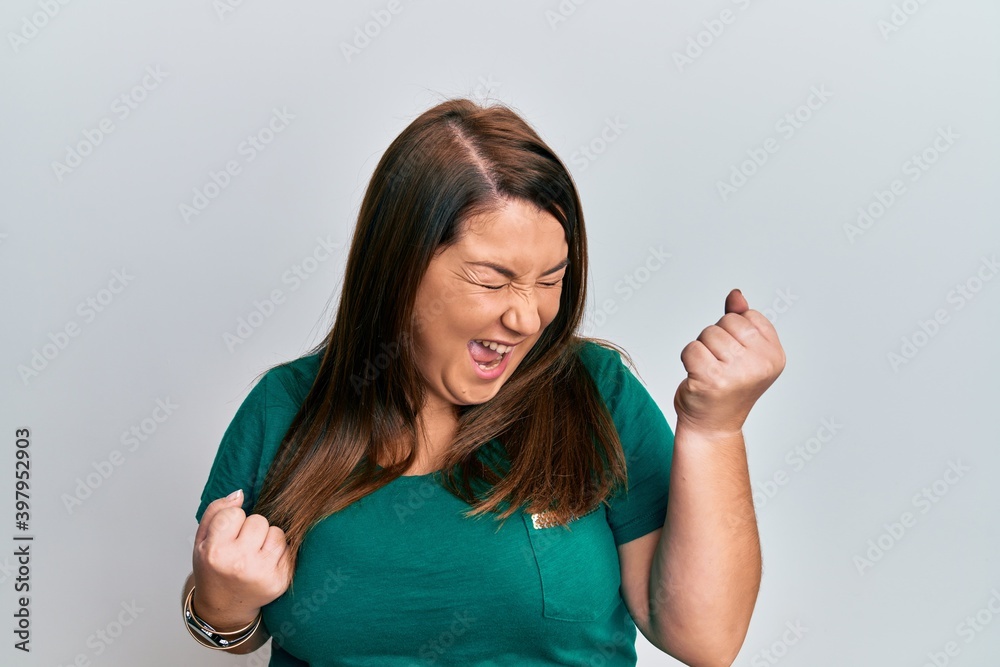 Beautiful brunette plus size woman wearing casual clothes celebrating surprised and amazed for success with arms raised and eyes closed Beautiful brunette plus size woman wearing casual clothes celebrating surprised and amazed for success with arms raised and eyes closed