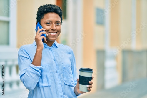 Young african american girl talking on the smartphone and drinking take away coffee at the city.