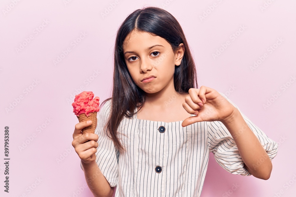 Beautiful child girl holding ice cream with angry face, negative sign showing dislike with thumbs down, rejection concept Beautiful child girl holding ice cream with angry face, negative sign showing dislike with thumbs down, rejection concept