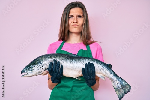 Beautiful caucasian woman fishmonger selling fresh raw salmon skeptic and nervous, frowning upset because of problem. negative person.