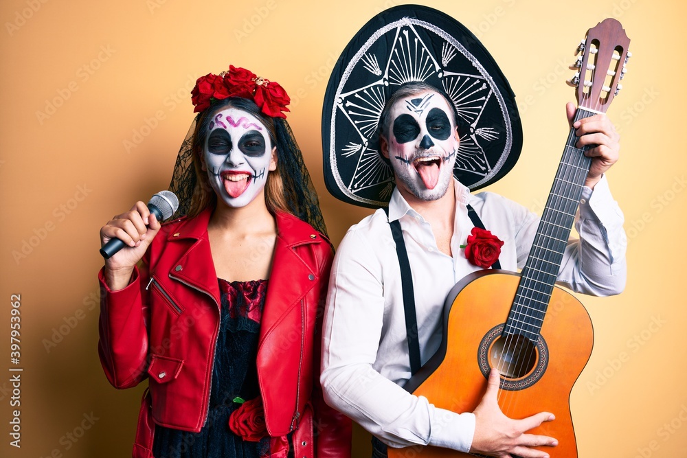 Couple wearing day of the dead costume playing classical guitar using microphone sticking tongue out happy with funny expression.
