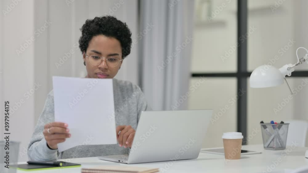 African Woman Reading Documents while using Laptop African Woman Reading Documents while using Laptop