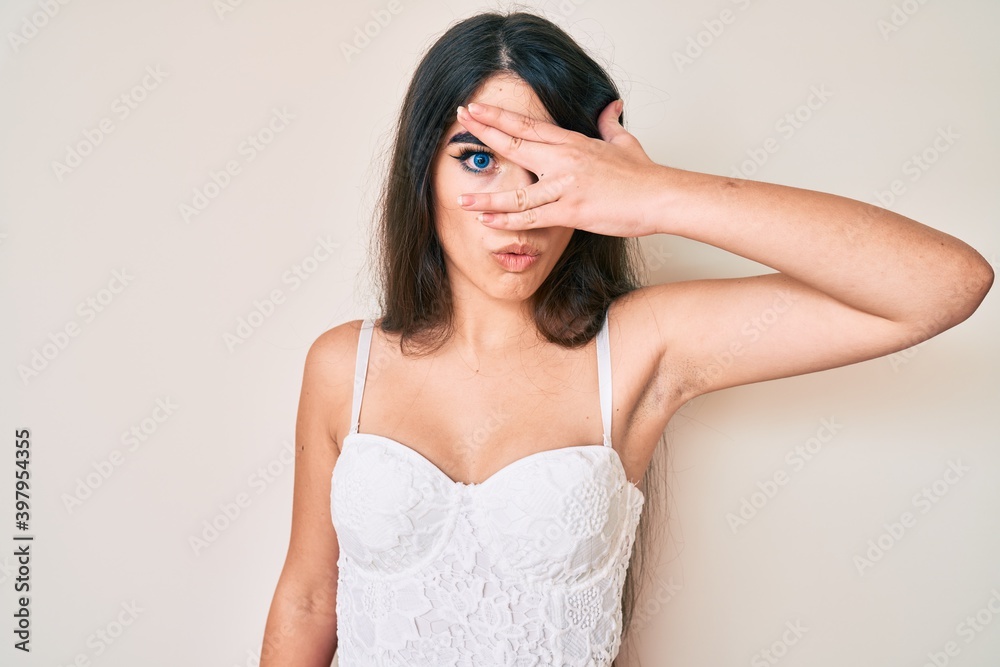 Brunette teenager girl posing elegant peeking in shock covering face and eyes with hand, looking through fingers with embarrassed expression. Brunette teenager girl posing elegant peeking in shock covering face and eyes with hand, looking through fingers with embarrassed expression.