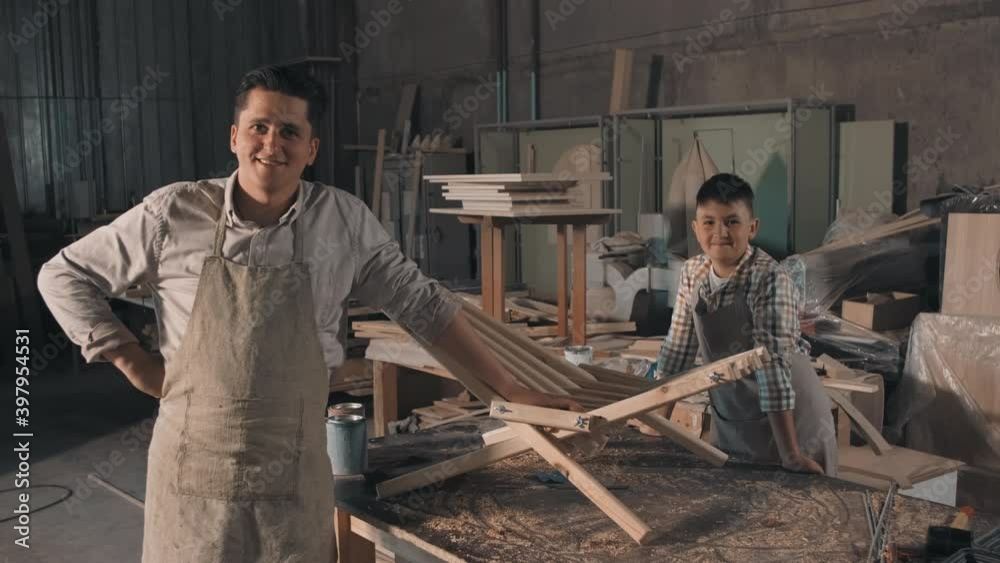 Medium portrait of two cheerful craftsmen in aprons just made wooden diy deck chair together in small carpentry Medium portrait of two cheerful craftsmen in aprons just made wooden diy deck chair together in small carpentry