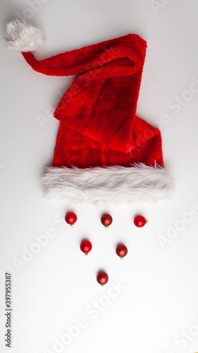 Red fluffy velvet Christmas Santa Claus hat with white tip and rim and red frosted bright Christmas balls on isolated white background. Holidays and greeting card concept composition with copy space.