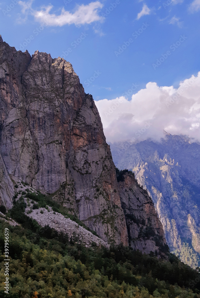 Summer view on a steep rocky slope of a mountain in a majestic gorge with white clouds in blue sky