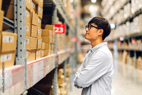 Portrait of smiling asian manager worker man standing and order details checking goods and supplies on shelves with goods background in warehouse.logistic and business export