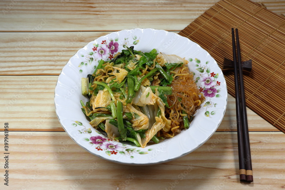 Fried and stirred instant noodle mixed with vermicelli and local herbal vegetable on the plate. Fusion vegetarian menu in Asia restaurant. Fried and stirred instant noodle mixed with vermicelli and local herbal vegetable on the plate. Fusion vegetarian menu in Asia restaurant.