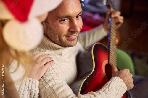 Confident male in warm sweater and beautiful female in Santa hat spending winter holidays in living room