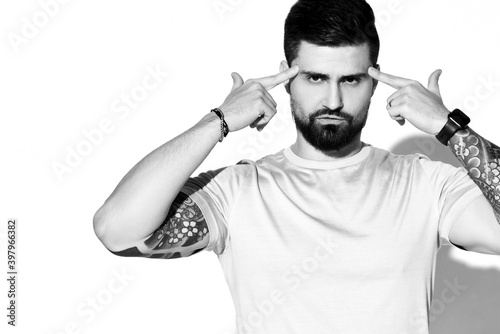 Portrait of bearded man fun guy with tattoo on arms in t-shirt looking at camera pointing at his forehead shooting thinking over white background. Hipster stylish look for free lifestyle concept