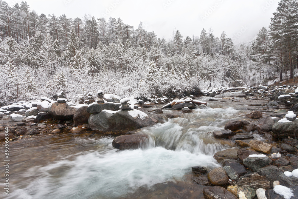 Beautiful fast mountain river and snowy white forest in snowfall and foggy day. Winter landscape. Cyclone, precipitation and bad weather. Christmas holidays in the highlands. Natural background Beautiful fast mountain river and snowy white forest in snowfall and foggy day. Winter landscape. Cyclone, precipitation and bad weather. Christmas holidays in the highlands. Natural background