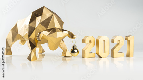 Golden volumetric paper bull with a Christmas ball on the horn and numbers 2021 on a white glossy background, symbol of the year