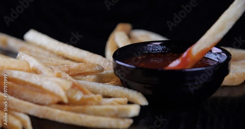 Hands arms human finger taking french fries and dipping gold yelow slise of potato in ketchup - macro closeup, top view. Cropped shot of fast food lying on table and on black background in pub cafe photo