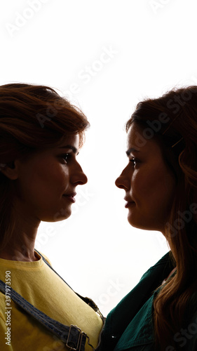 Cropped shot of two young girls, twin sisters looking at each other, posing together, standing face to face isolated over white background