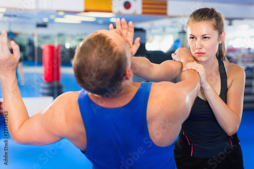 Strong positive cheerful woman is training with man on the self-defense course in gym.