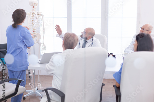 Expert doctor in radiology pointing at human skeleton during presentation in hospital conference room. Clinic therapist talking with colleagues about disease  medicine professional.