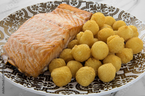 Gourmet gastronomy. Closeup view of a delicious baked salmon filet with fried noisette potatoes garnish, served on a decorated deep plate. photo