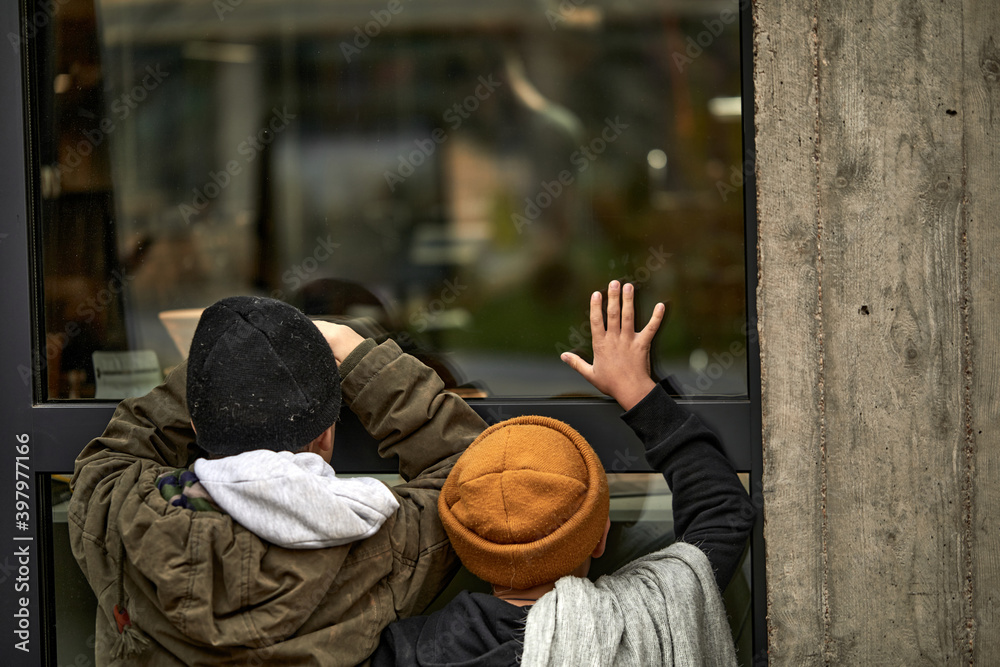 rear view on two poor homeless children leaned on window of building, need shelter and food