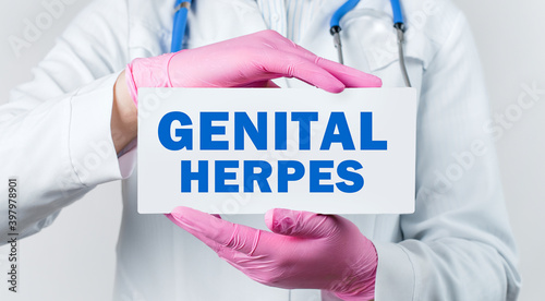 Cropped view of female doctor in a white coat and pink sterile gloves holding a card with words - GENITAL HERPES photo
