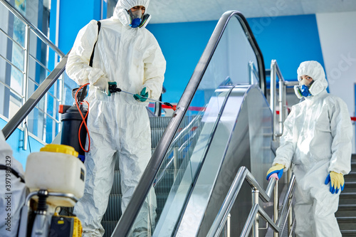 brave disinfectors sterilising the escalator and shopping mall building, work together, use sprays sterilizing the area