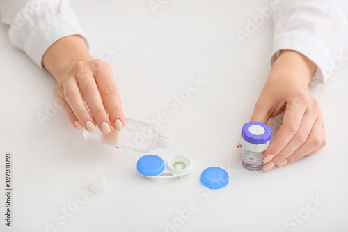 Woman pouring solution in container with contact lenses on white background