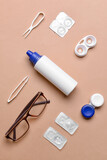 Containers with contact lenses, solution, tweezers and eyeglasses on color background
