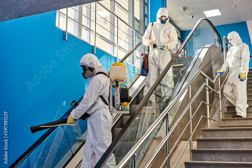 workers in hazmat suit making disinfection indoors on escalator, coronavirus decontamination for people healthcare