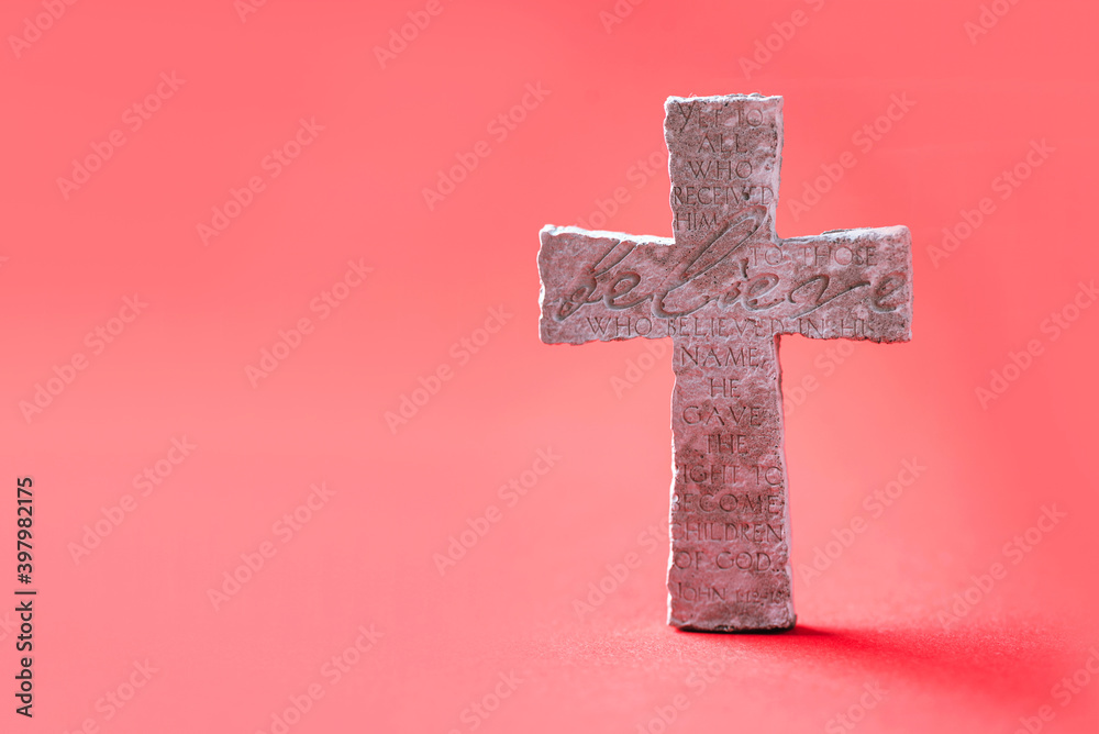 Stone cross with inscription Believe on red background, Copy space. Christian backdrop. Biblical faith, gospel, salvation concept