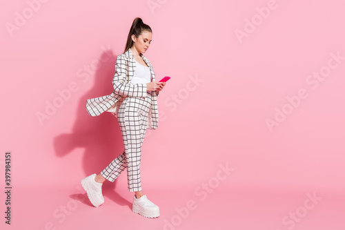 Photo portrait full body view of woman walking texting holding phone in two hands isolated on pastel pink colored background