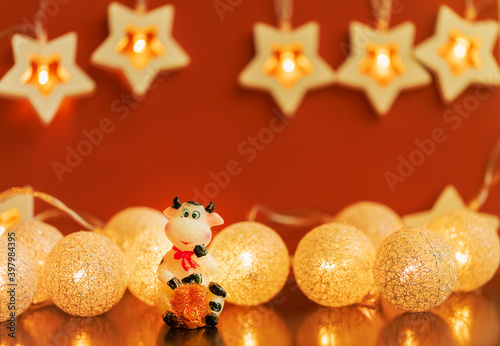 Bull on a dark background with garlands. Statuette of a cow with a bag of money on a brown background. Christmas, New Year 2021, symbol of the year. Copy space.