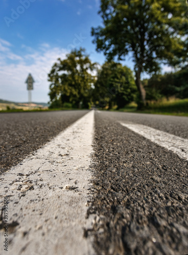 Wide angle shot of white line road marking disappearing into the distance on a sunny day.