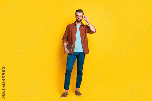 Full length photo of young business man confident serious hold laptop hand touch glasses isolated over yellow color background