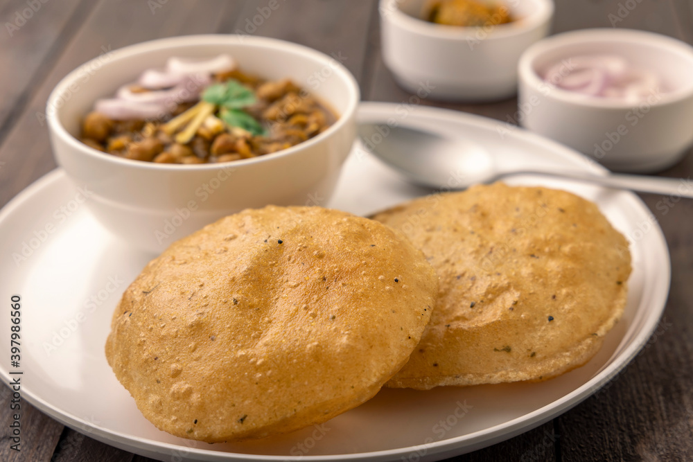 Spicy chick peas curry or Chana Masala or choley with fried puri garnished with sliced onion and green coriander leaf