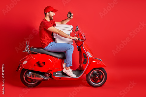 handsome courier guy on motorbike is hurry to deliver orders  check the time  delivery  food  restaurant concept. isolated red background