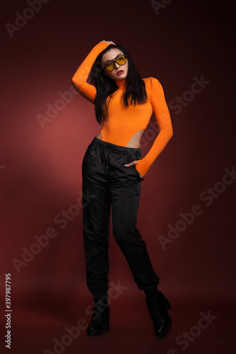 beautiful girl in sunglasses and an orange sweater posing in the studio on a red background