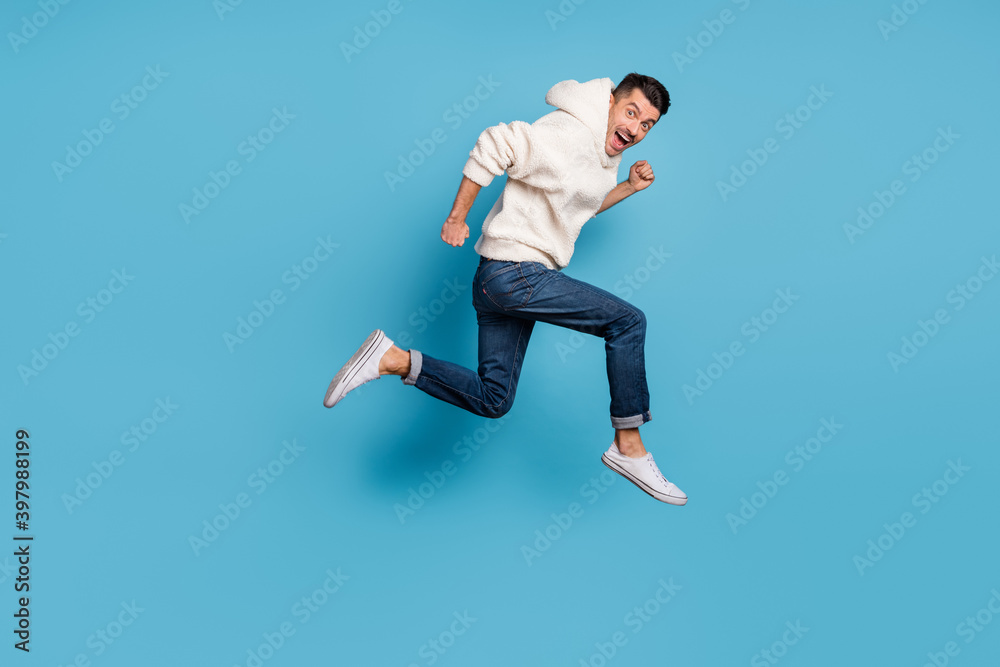 Full size profile side photo of young happy excited smiling positive man running jumping isolated on blue color background