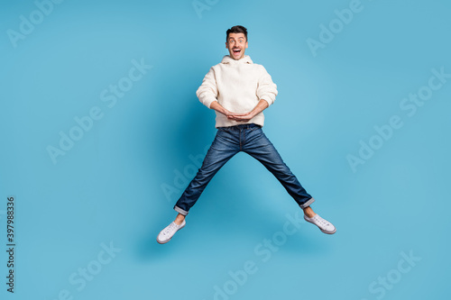 Photo portrait full body view of funny guy jumping up spreading legs like star wearing woolen hoodie isolated on pastel blue colored background
