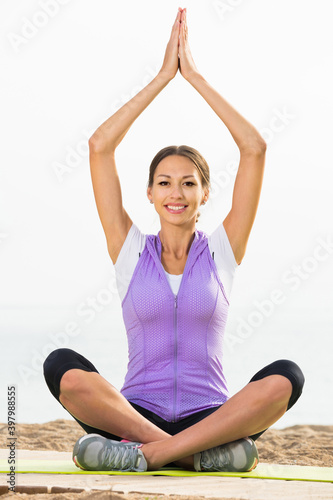 Young smiling woman practise yoga cross-legged in morning by sea