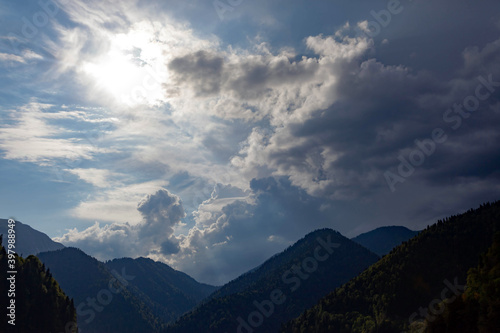Beautiful green mountains with trees in the sun against the blue sky with clouds, used as a background or texture
